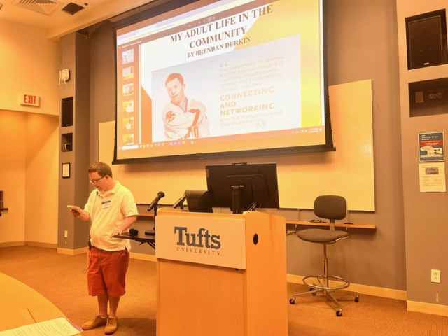 a man standing at a podium in front of a projector screen