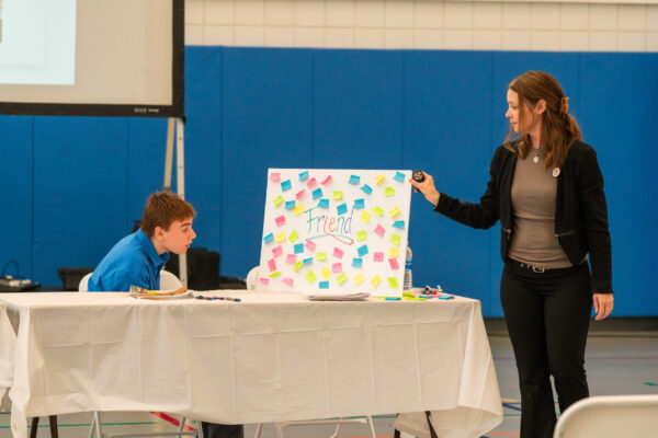 a woman standing next to a boy at a table