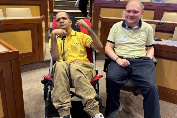 a man sitting in a wheel chair next to another man