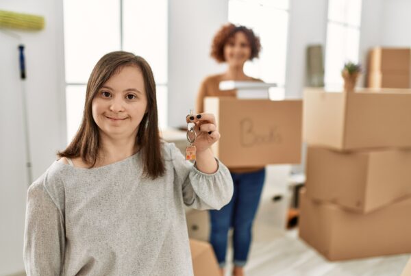 Mature mother and down syndrome daughter moving to a new home, standing by cardboard boxes showing house key chain