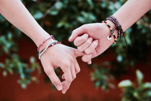 Two hands wearing friendship bracelets, linking pinkies.