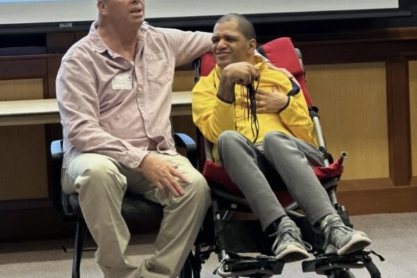 a man sitting in a wheel chair next to another man