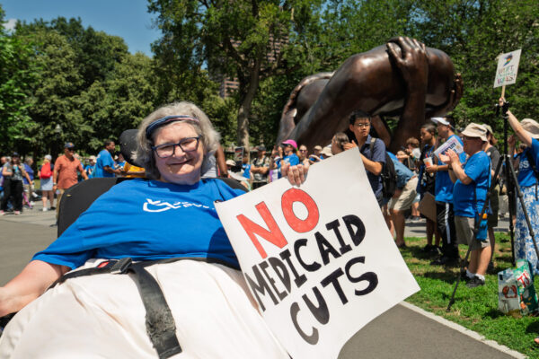 a woman in a wheel chair holding a sign that says no medicaid cuts
