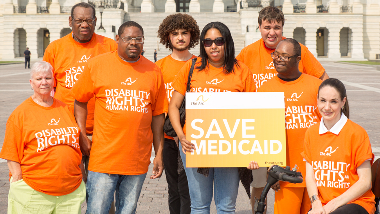 a group of people in orange shirts holding a save medicaid sign