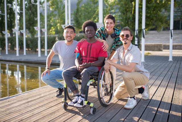 4 friends, one of whom uses a wheelchair, smiling and posing for a picture