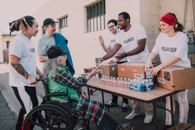 Three people behind a table handing out water to three other people, one of whom uses a wheelchair