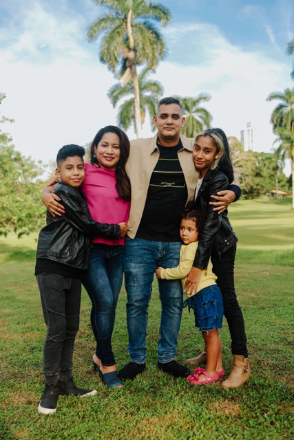 A family with a mother, father and three children posing for a picture, in front of a palm tree