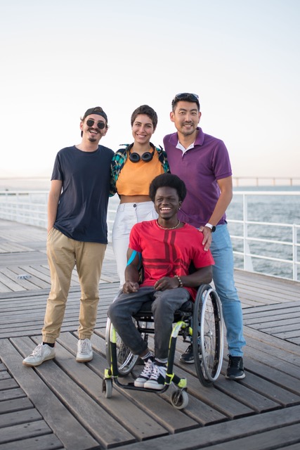 Four friends, one in a wheelchair smiling on a pier