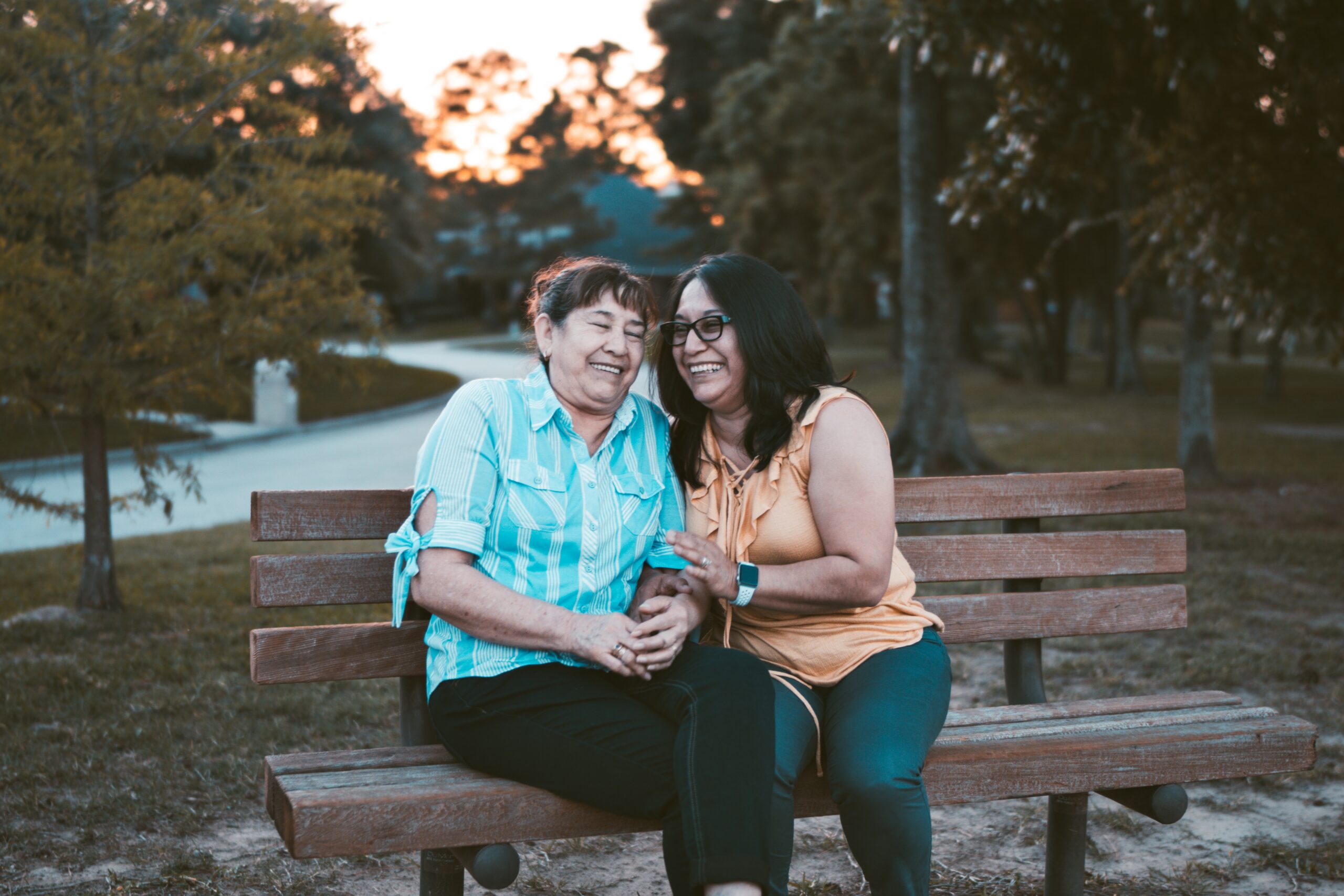 An older and younger woman sitting on a bench and laughing